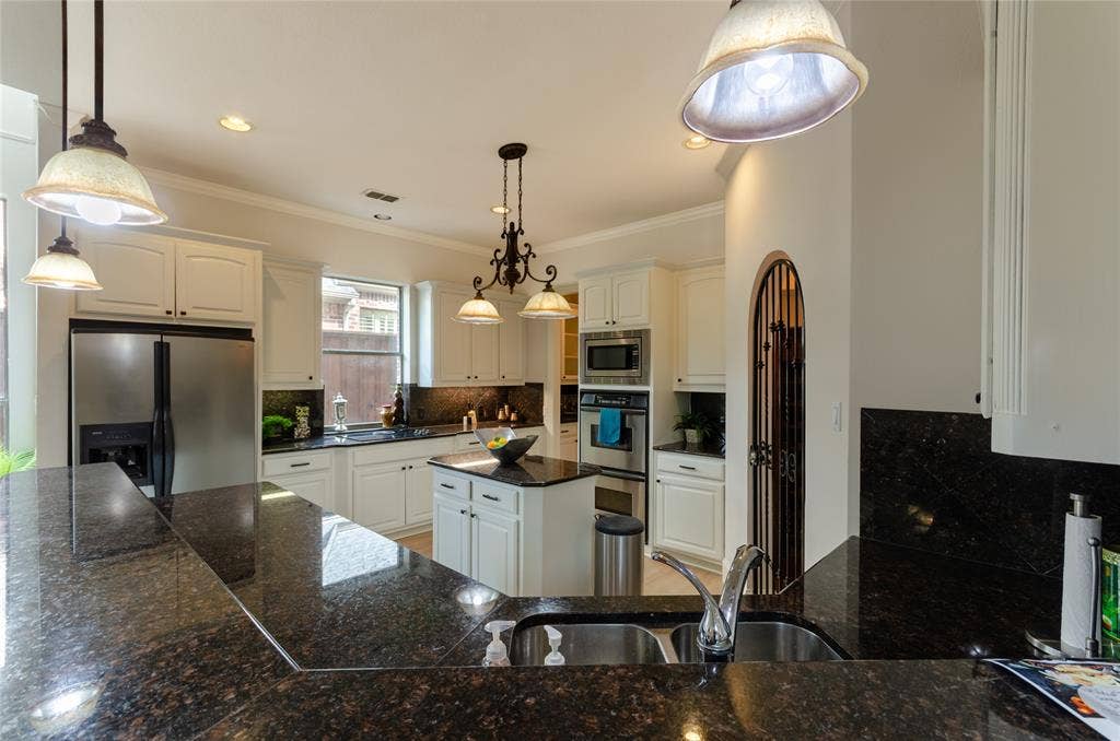 Kitchen featuring stone countertops, stainless steel built-in double ovens, a center island, white cabinetry, and decorative pendant lighting
