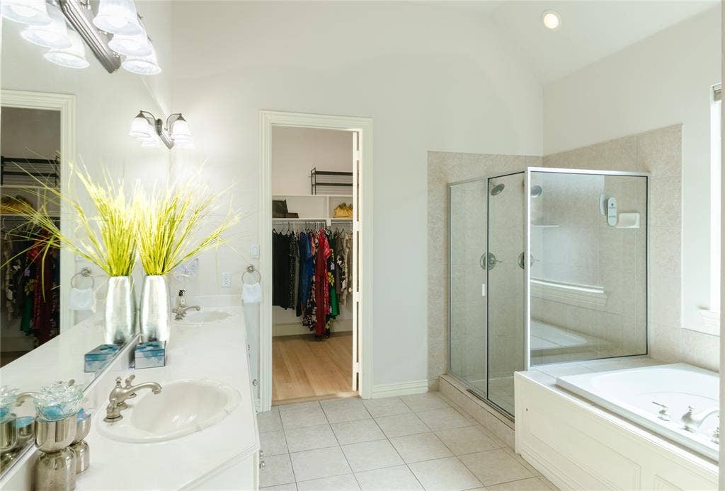 Double vanity with a solid-surface countertop, walk-in shower with a glass enclosure, built-in soaking tub, and ceramic tile flooring
