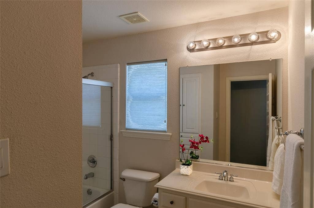 Bathroom featuring a vanity with a solid-surface countertop, rectangular undermount sink, multi-bulb wall-mounted light fixture, large wall-mounted mirror, and a tub-shower combination with sliding glass doors