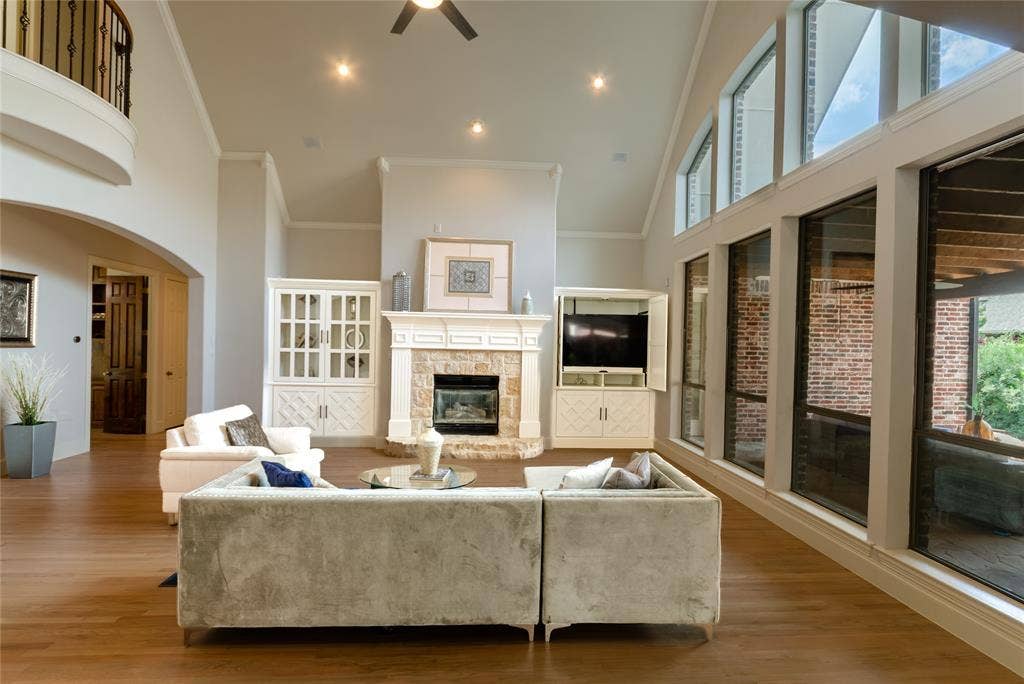 Vaulted ceilings with recessed lighting, stone-surround fireplace, built-in cabinetry, wood-finish flooring, and expansive windows