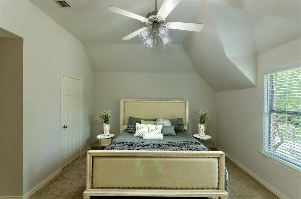 Vaulted ceilings, neutral wall color palette, carpeted flooring, window with slatted blinds, and ceiling fan with integrated light fixture