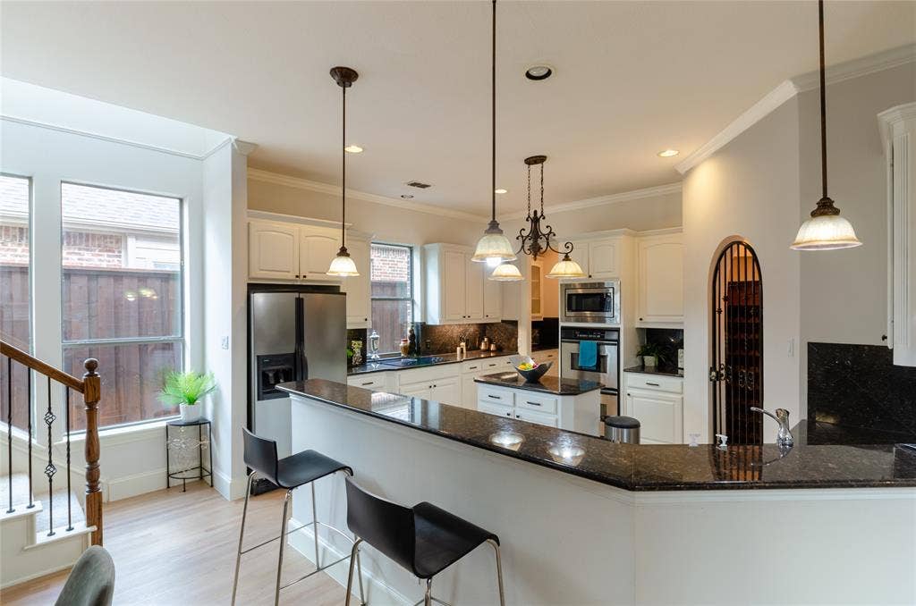 Kitchen featuring a multi-level stone-surface breakfast bar, white cabinetry, integrated stainless steel appliances, a center island, and arched doorway with decorative metal gate