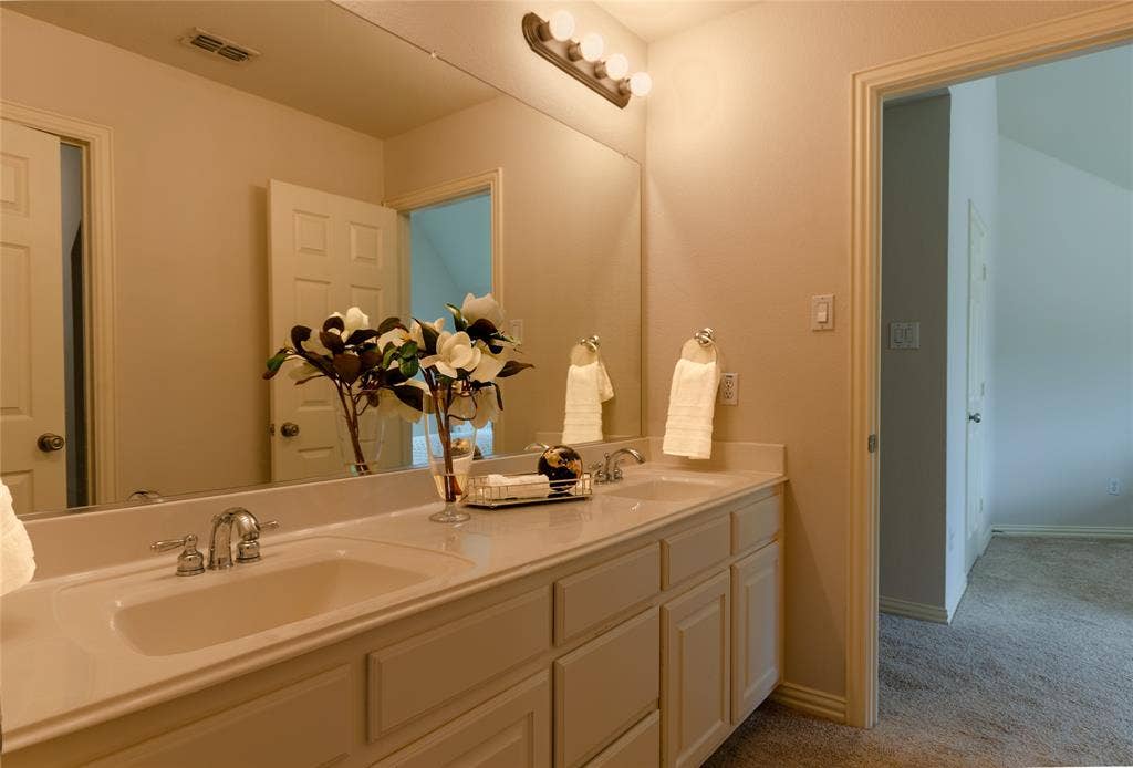 Dual-sink vanity featuring integrated stone-top basins, extensive wall-spanning mirror, custom cabinetry, and polished chrome fixtures