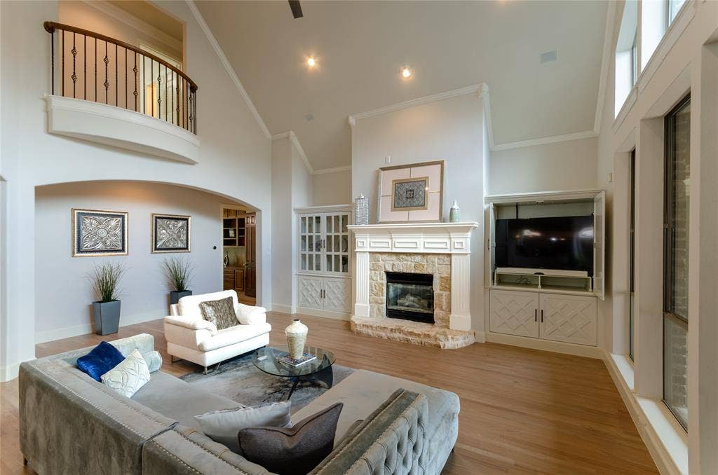 Vaulted ceilings with an overlook balcony, stone-faced fireplace with a detailed mantel, wood-finish flooring, and built-in custom cabinetry