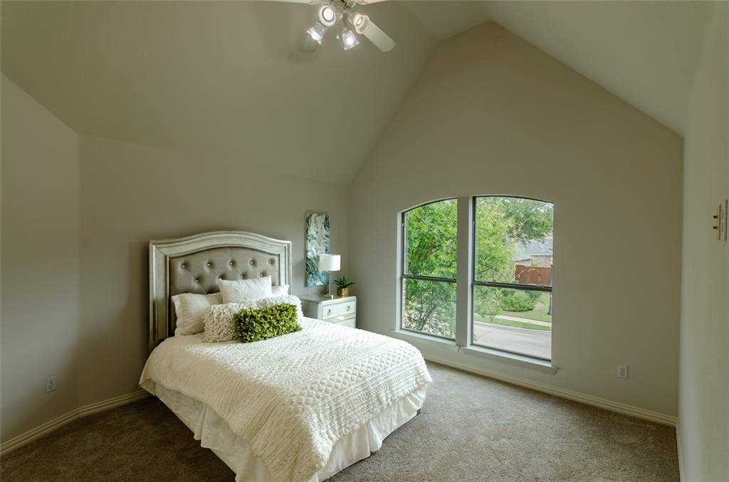 High vaulted ceiling with neutral paint, carpeted flooring, and a large arched window