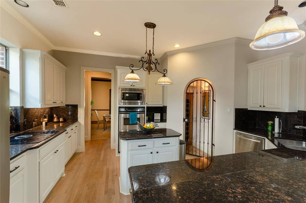 Kitchen featuring white cabinetry, stone countertops, stainless steel wall-mounted oven and microwave, wood-finish flooring, and a decorative arched metal gate