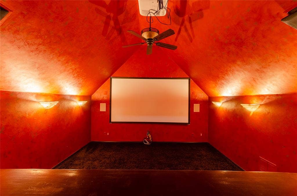 Vaulted ceiling featuring a central ceiling fan, fixed projection screen, and wall-mounted sconce lighting