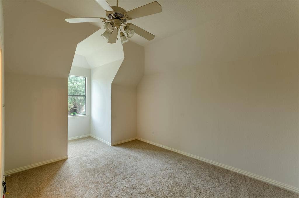 Bedroom Vaulted ceiling featuring an integrated multi-blade ceiling fan with a triple-light fixture, expansive recessed window alcove, and neutral wall-to-wall carpeting
