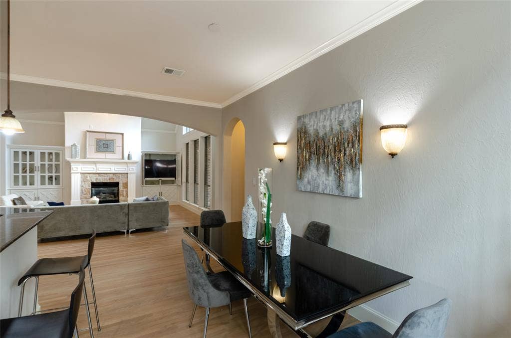 Open-concept interior featuring light wood-finish flooring, crown molding, arched entryways, and two wall-mounted decorative light fixtures