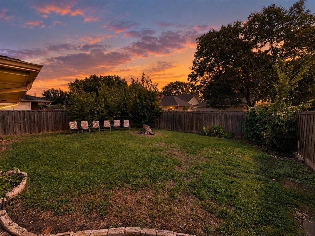 3408 Bellah Court, Irving, TX 75062 Expansive backyard featuring a manicured lawn, stone-border garden beds, mature trees, and perimeter wood fencing
