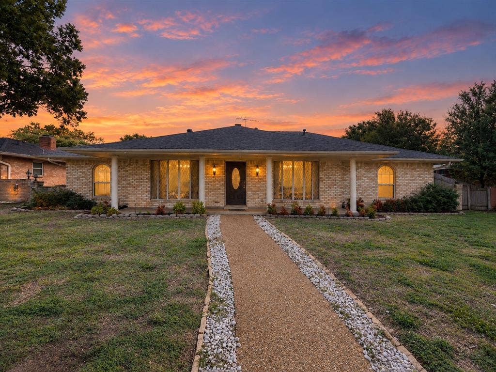 3408 Bellah Court, Irving, TX 75062 Single-story brick exterior featuring a covered front porch with white columns, arched window detailing, and a stone-bordered gravel walkway