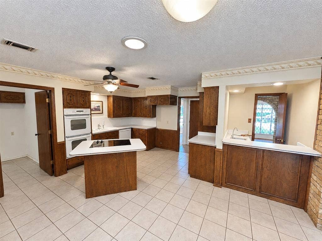 3408 Bellah Court, Irving, TX 75062 Kitchen featuring wood cabinetry, integrated double wall ovens, a center island with a cooktop, a pass-through bar, and tile flooring