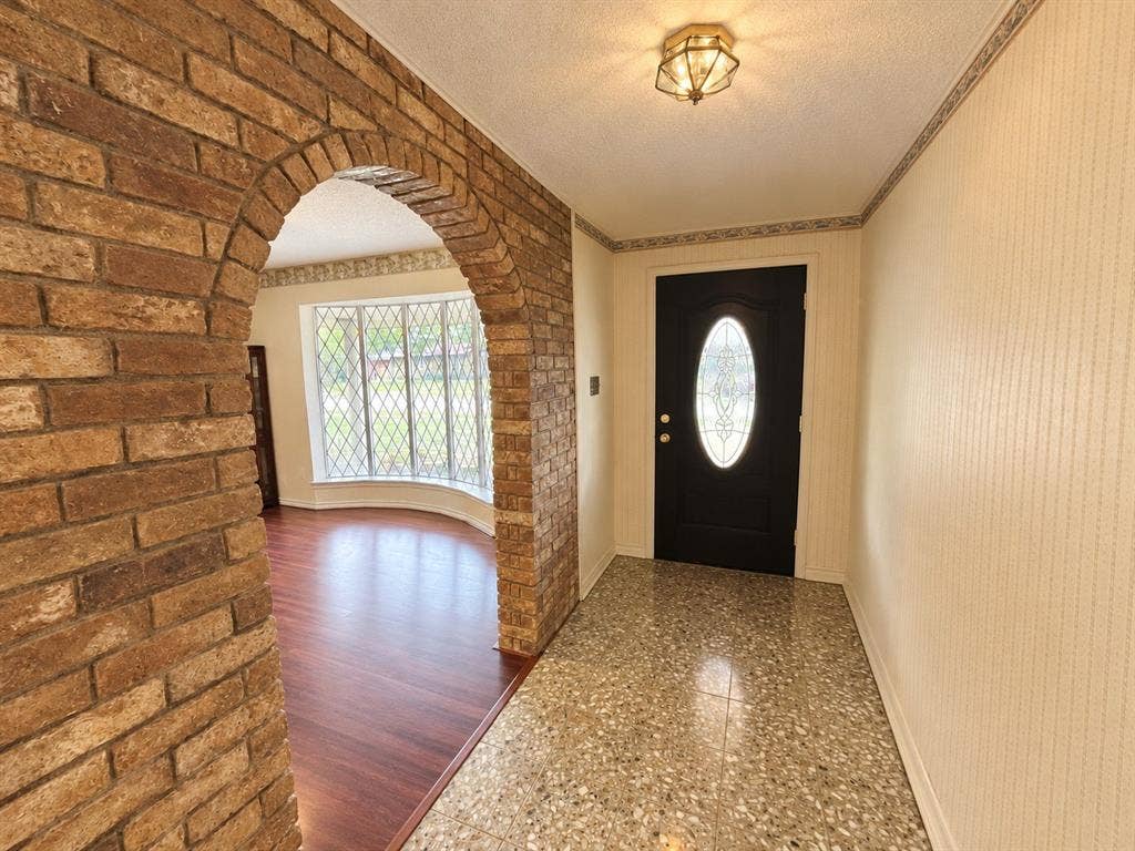 3408 Bellah Court, Irving, TX 75062 Entryway featuring a structural brick arch, diamond-pane bay window, solid-core front door with decorative oval glass inlay, wood-finish flooring, and terrazzo tile flooring