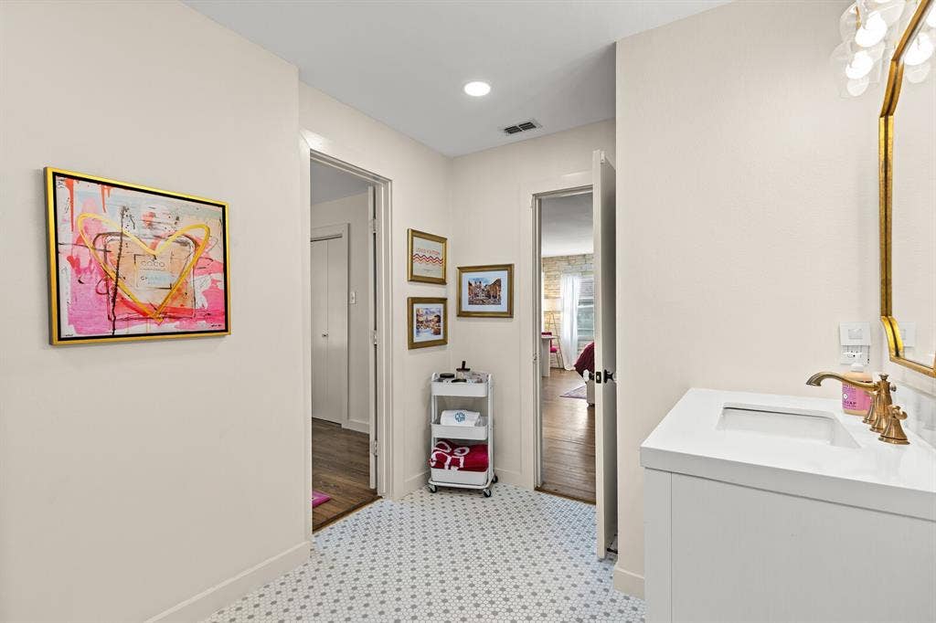 2425 S 2nd Street, Waco, TX 76706 Bathroom featuring a vanity with a rectangular sink, brass-tone faucet, geometric hexagonal tile flooring, and a decorative gold-framed wall mirror