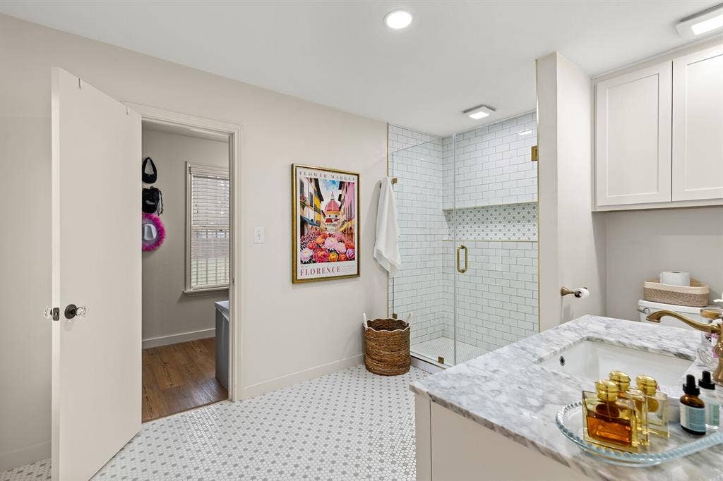 2425 S 2nd Street, Waco, TX 76706 Bathroom featuring a stone-surface vanity with an integrated sink, shower enclosure with white subway tile surround, patterned mosaic floor tile, and shaker-style cabinetry