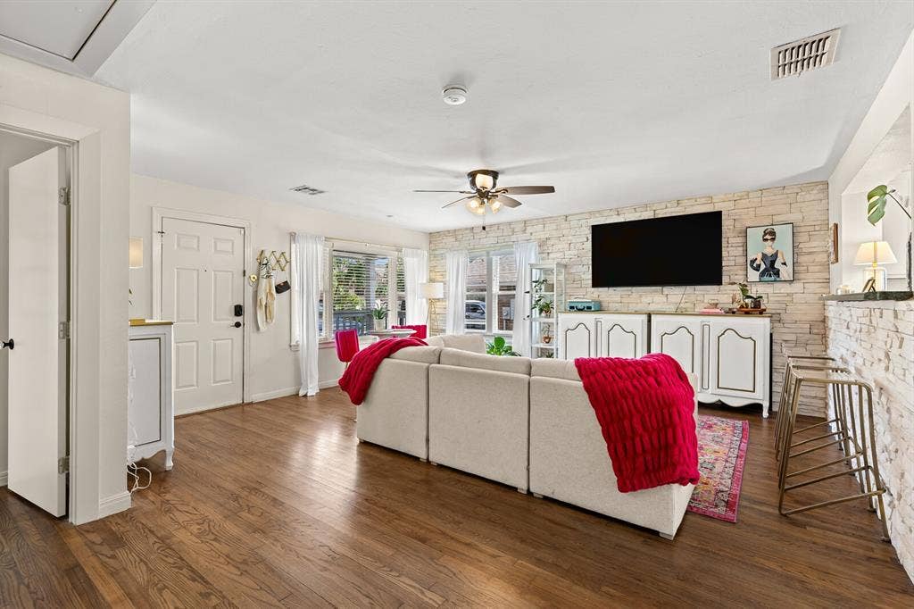 2425 S 2nd Street, Waco, TX 76706 Living area featuring wood-finish flooring, a light-toned stone accent wall, multi-pane windows, and a ceiling fan with integrated light fixture
