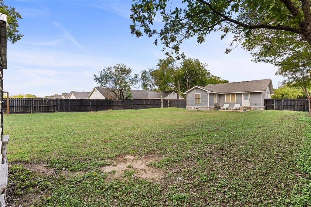 2425 S 2nd Street, Waco, TX 76706 Expansive backyard featuring a large grass lawn, perimeter wood privacy fencing, a stone-accented exterior foundation, and mature trees