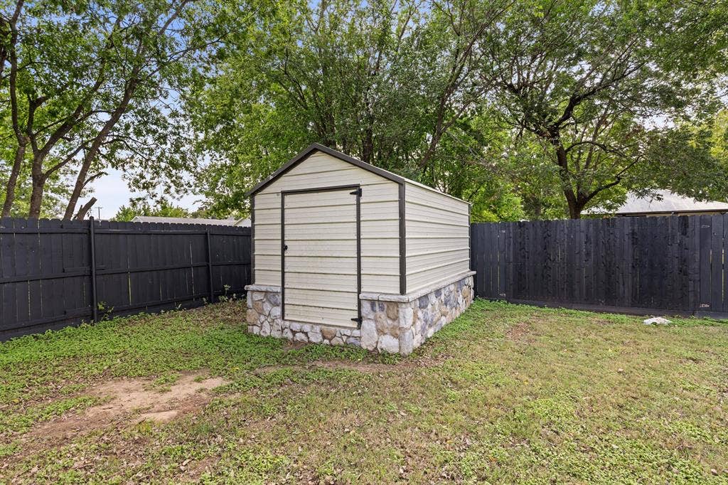 2425 S 2nd Street, Waco, TX 76706 Exterior storage structure featuring a metal-sided frame, a stone masonry foundation, and a gabled roof, enclosed within a black perimeter fence
