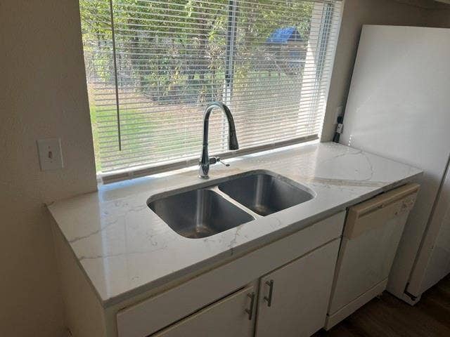1236 Neptune Drive, Cedar Hill, TX 75104 Dual-basin stainless steel sink featuring a high-arc pull-down faucet, white stone-patterned countertop, and white under-counter cabinetry with metallic hardware