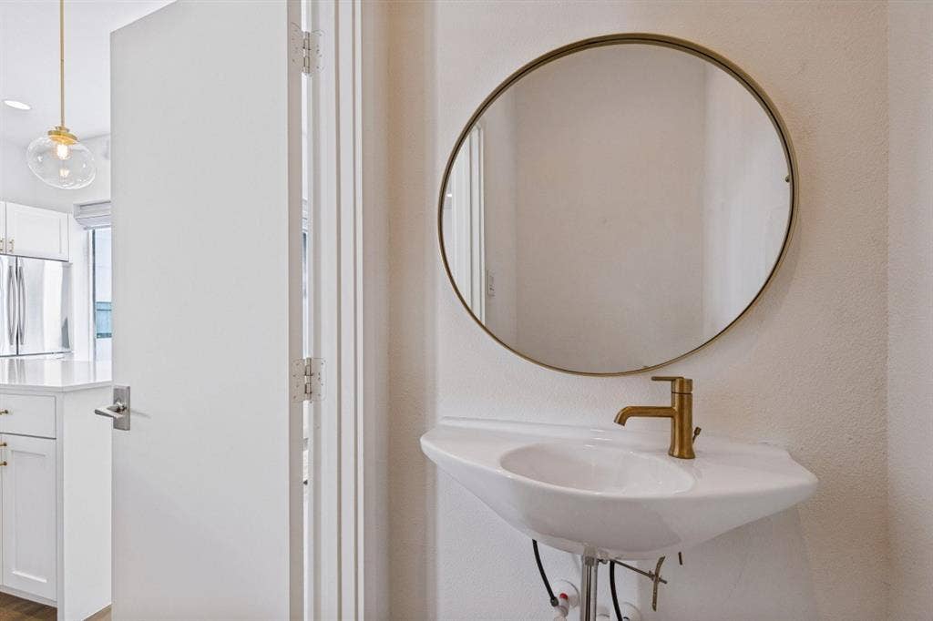 2107 Bennett Avenue, #20, Dallas, TX 75206 Wall-mounted pedestal sink with a brass-finish faucet, paired with a circular mirror featuring a brass-tone frame