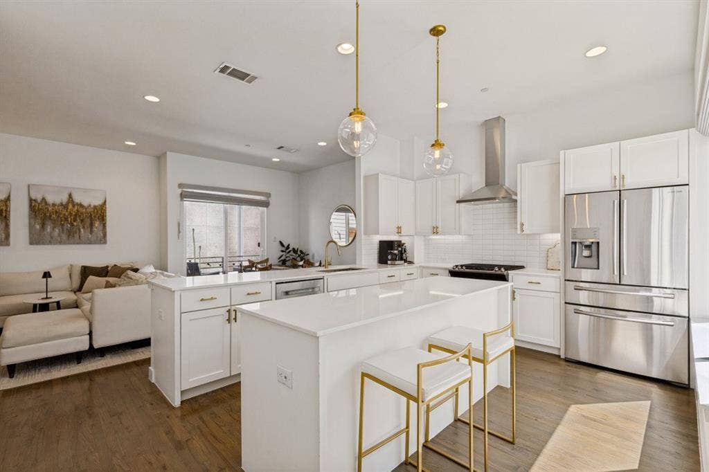 2107 Bennett Avenue, #20, Dallas, TX 75206 Kitchen featuring an oversized central island with quartz countertops, white shaker-style cabinetry, stainless steel appliances, and dual glass pendant lights set against wood-finish flooring