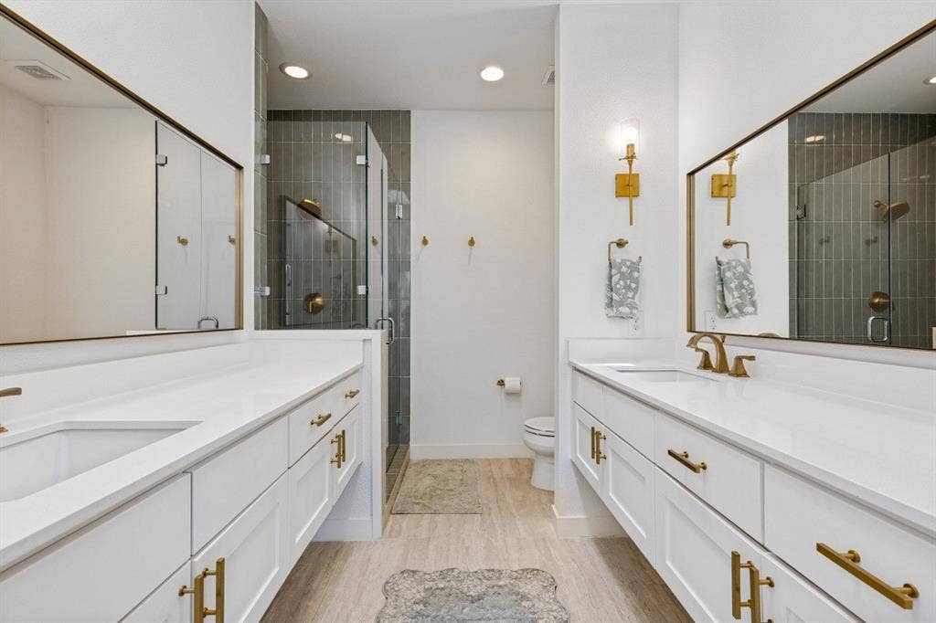 2107 Bennett Avenue, #20, Dallas, TX 75206 Dual vanities featuring white cabinetry, solid surface countertops, metallic hardware, large rectangular mirrors, and a glass-enclosed shower with vertical wall tiling