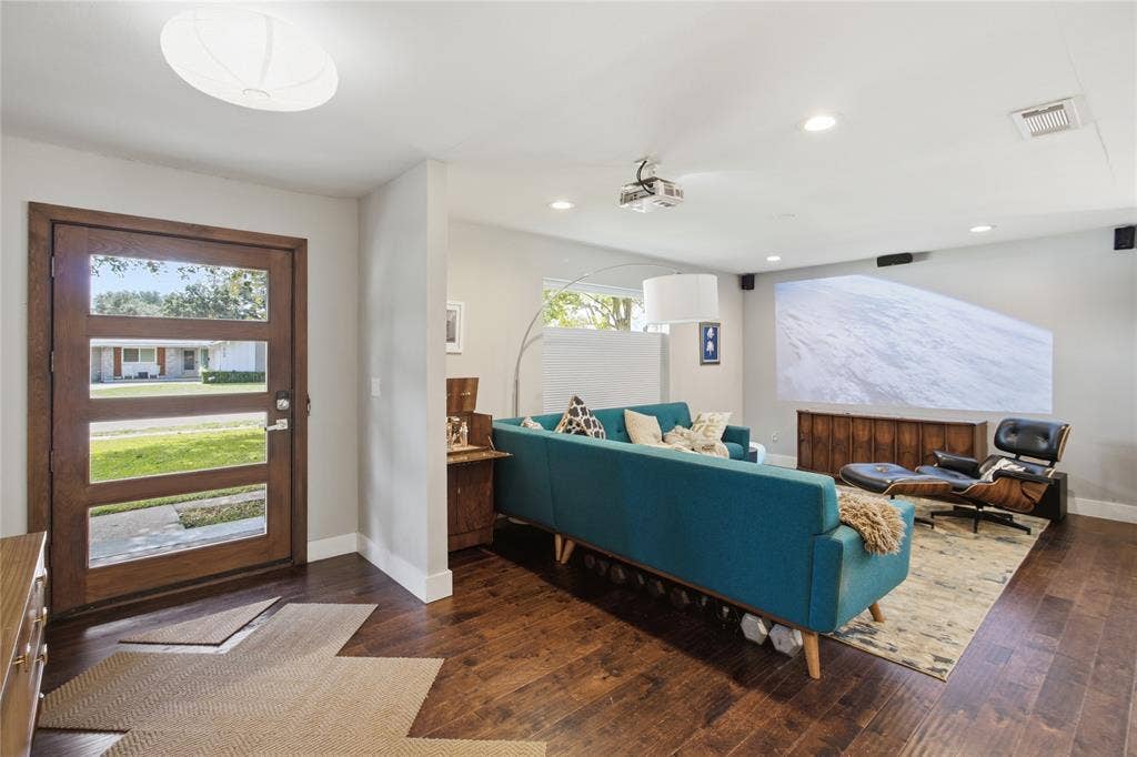 2712 Beechmont Place, Dallas, TX 75228 Step inside and discover a welcoming entry that opens into a stylish living room with mid-century modern influences. Rich, warm-toned flooring, clean architectural lines, and abundant natural light create an inviting atmosphere. The living area features a ceiling-mounted projector and speakers, creating a home theater experience for movie nights, sporting events, or relaxing at home. The combination of modern technology and comfortable living makes this a space designed to be enjoyed.