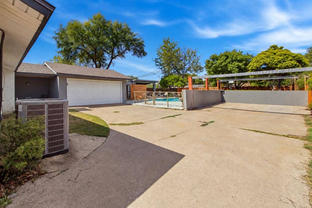 2712 Beechmont Place, Dallas, TX 75228 The expansive paved parking area provides additional space for vehicles beyond the attached two-car garage. Conveniently located at the end of the gated driveway, this versatile area offers flexibility for everyday parking and visiting guests. Decorative metal fencing separates the adjacent swimming pool and cabana area, helping define the property's distinct outdoor spaces.