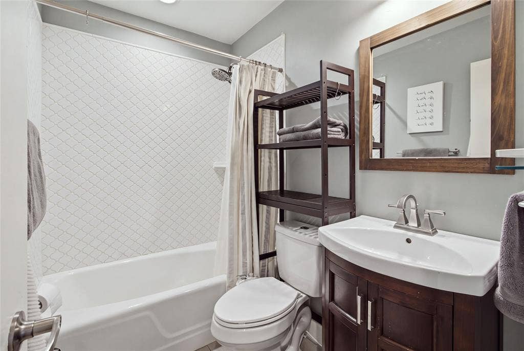2712 Beechmont Place, Dallas, TX 75228 The second full bathroom is conveniently located off the hallway, serving both secondary bedrooms and guests. Features include a tub and shower combination with decorative tile surround, a dark wood vanity, and a coordinating framed mirror.