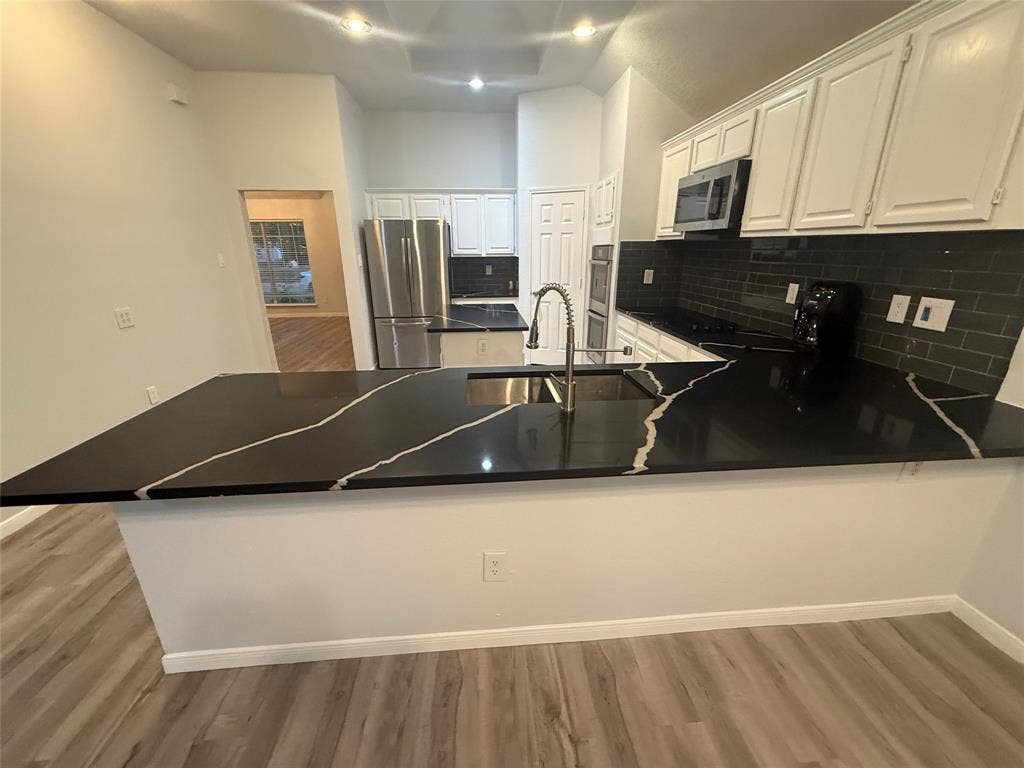 14 Heritage Way, Allen, TX 75002 Kitchen featuring black stone-patterned countertops, dark subway tile backsplash, white cabinetry, stainless steel appliances, and wood-finish flooring