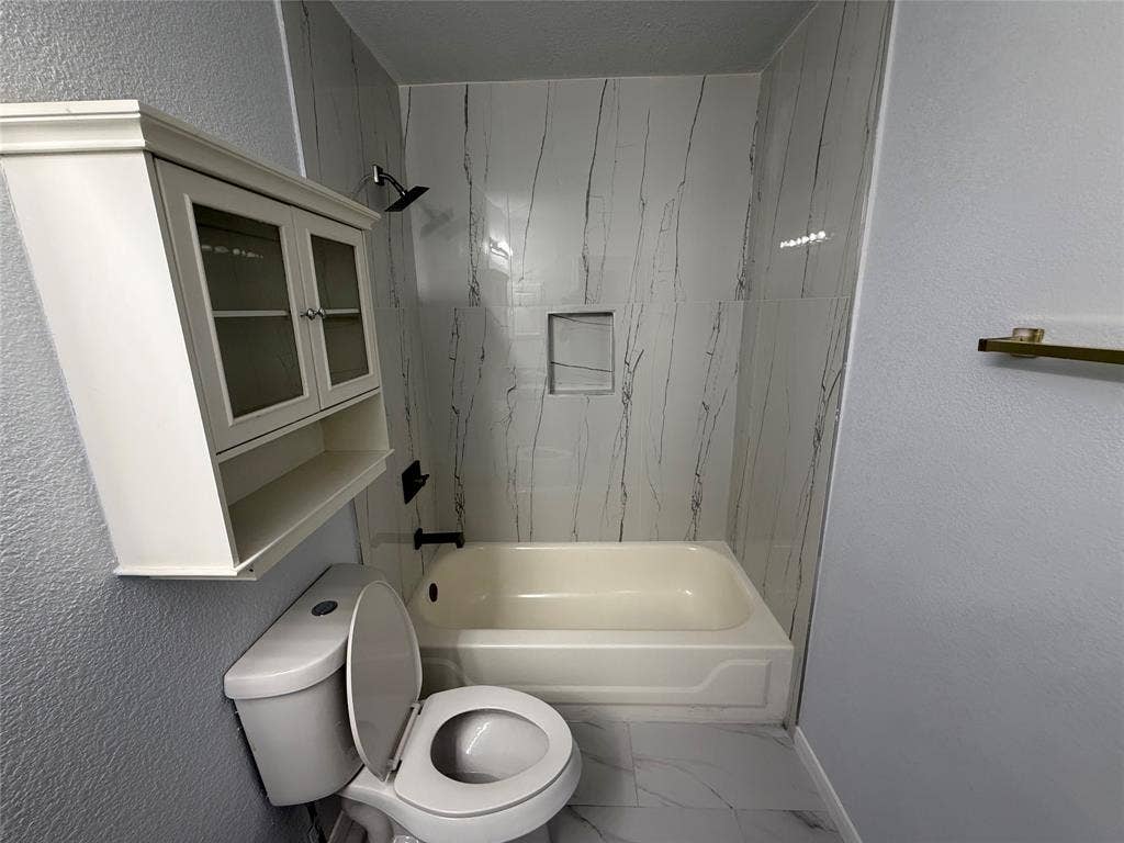 14 Heritage Way, Allen, TX 75002 Full-height shower surround with veined tile patterning, integrated wall niche, built-in wall-mounted cabinetry, matte black plumbing fixtures, and large-format tile flooring