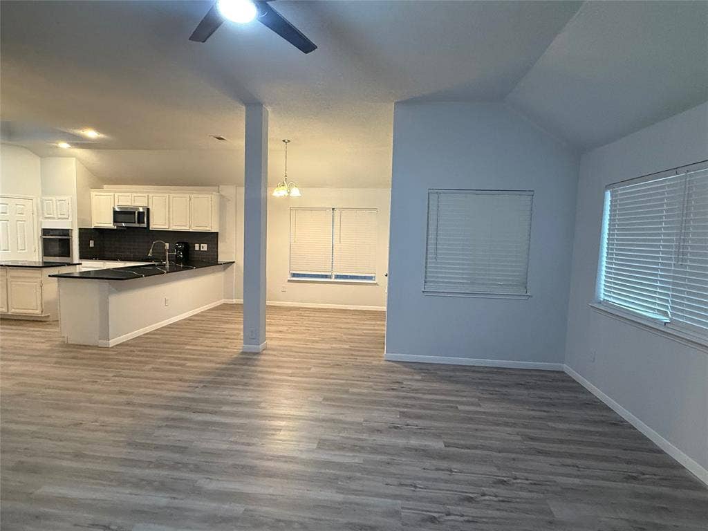 14 Heritage Way, Allen, TX 75002 Open-concept area featuring wood-finish flooring, vaulted ceilings, kitchen with black countertops, white cabinetry, and recessed lighting