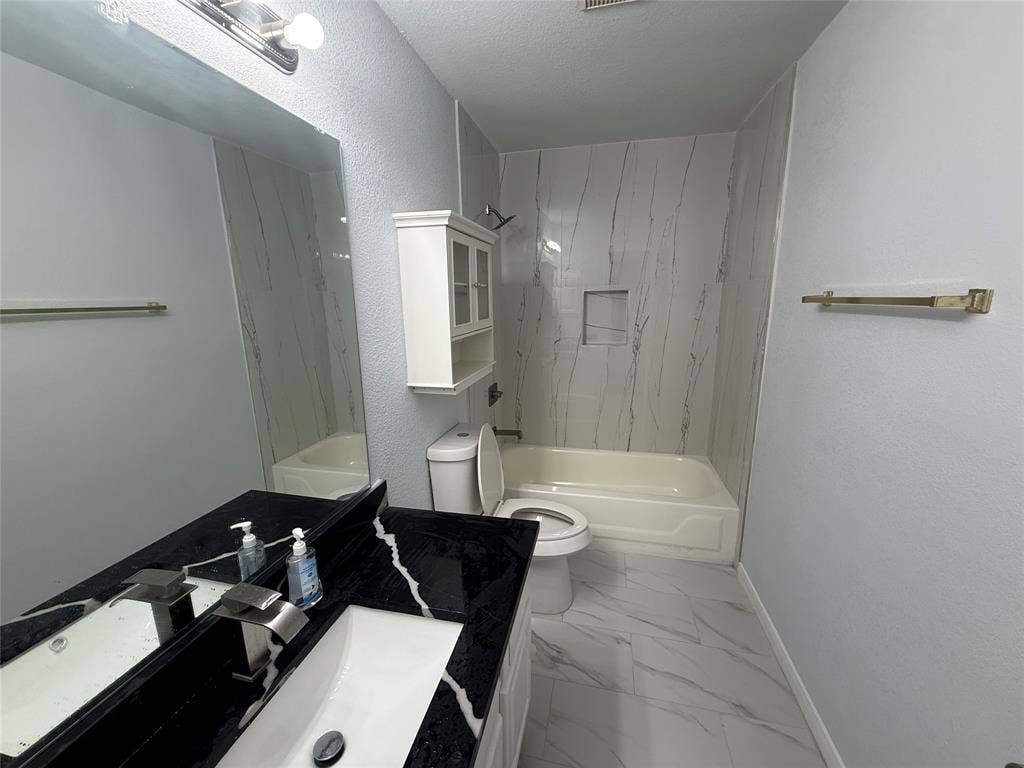 14 Heritage Way, Allen, TX 75002 Bathroom featuring a black vanity countertop with a white vessel sink, polished metal faucet, built-in storage cabinet, and large-format tile flooring with a shower-tub enclosure featuring tiled wall surrounds