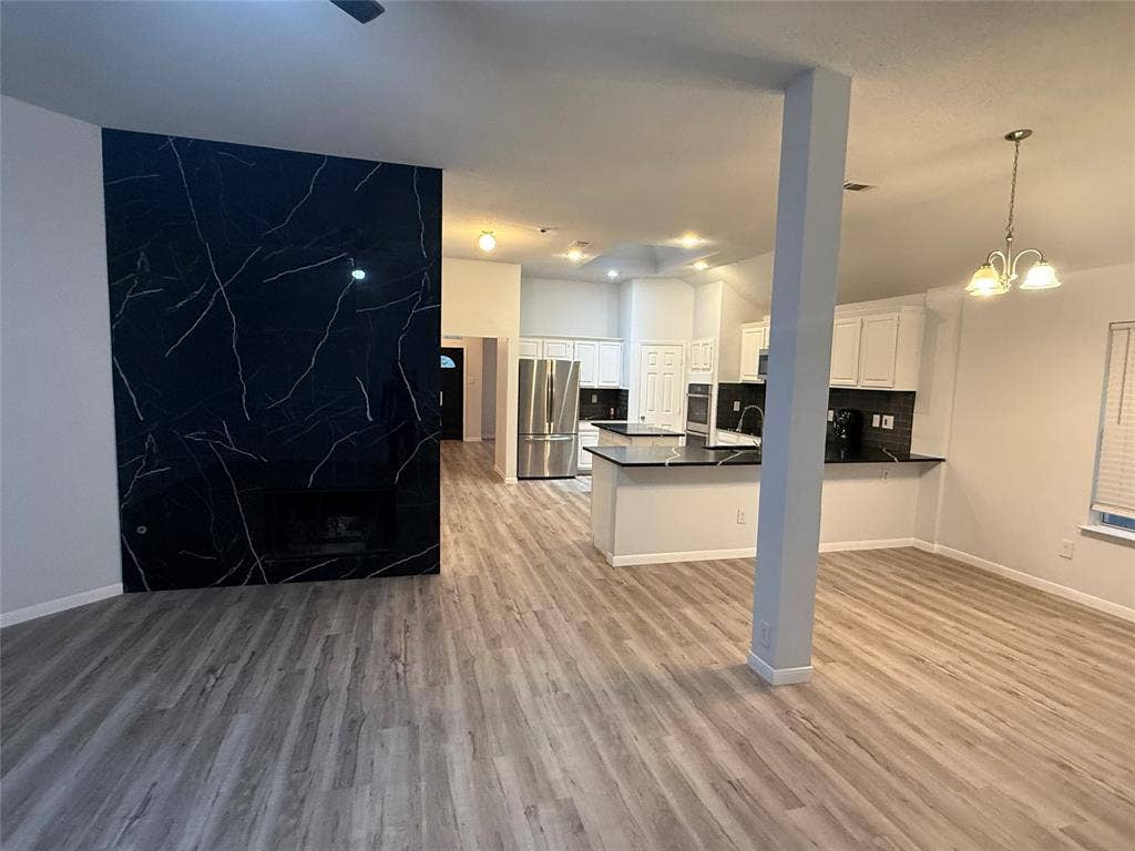 14 Heritage Way, Allen, TX 75002 Floor-to-ceiling dark-veined stone fireplace surround, wood-finish flooring, white cabinetry, integrated stainless steel appliances, and multi-bulb pendant lighting