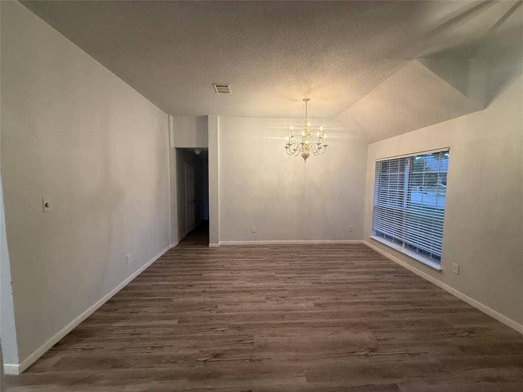 14 Heritage Way, Allen, TX 75002 Interior space featuring vaulted ceilings, wood-finish flooring, a multi-arm candle-style chandelier, and a large window with horizontal blinds