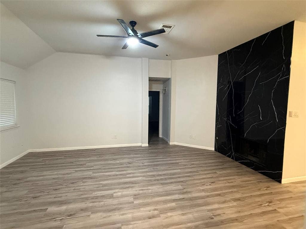 14 Heritage Way, Allen, TX 75002 Room featuring vaulted ceilings, wood-finish flooring, a matte black multi-blade ceiling fan, and a floor-to-ceiling black stone-patterned fireplace surround