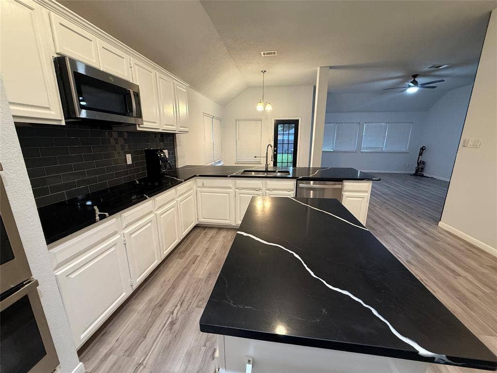 14 Heritage Way, Allen, TX 75002 Kitchen featuring white cabinetry, black stone countertops with prominent veining, stainless steel built-in microwave, charcoal subway tile backsplash, and wood-finish flooring