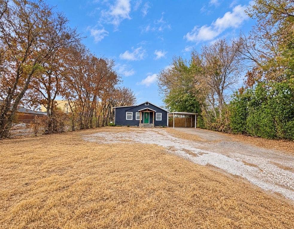 5512 Curzon Avenue, Fort Worth, TX 76107 Single-story exterior featuring dark lap siding, a covered carport, a gravel driveway, and mature perimeter trees
