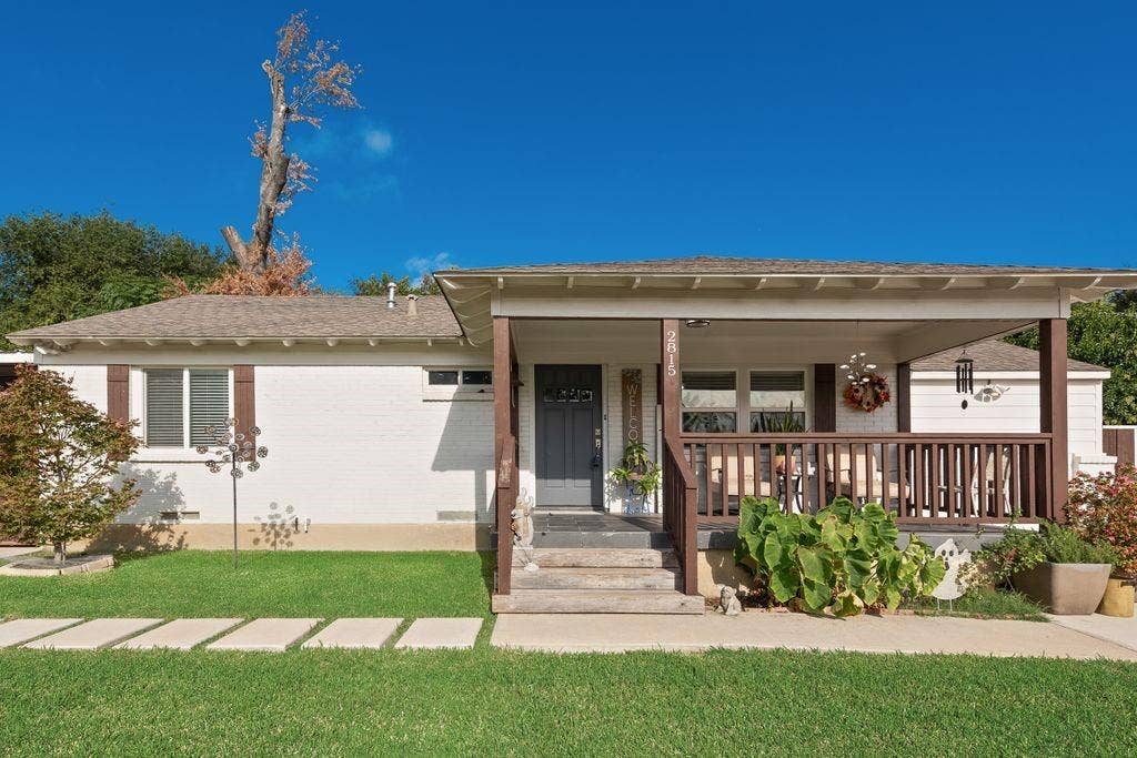 2815 Anzio Drive, Dallas, TX 75224 Painted brick exterior featuring a covered front porch, dark-toned wood railing, and a multi-paned entry door