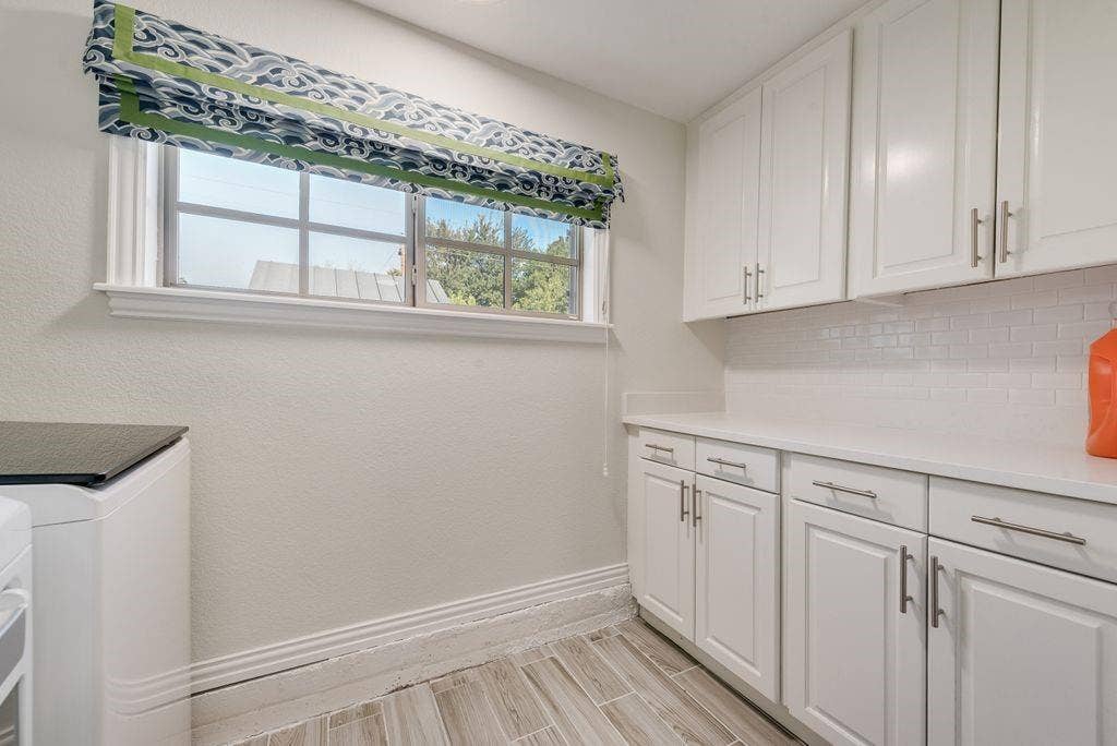 2815 Anzio Drive, Dallas, TX 75224 Laundry area featuring white shaker-style cabinetry, solid-surface countertops, white subway tile backsplash, and wood-finish tile flooring