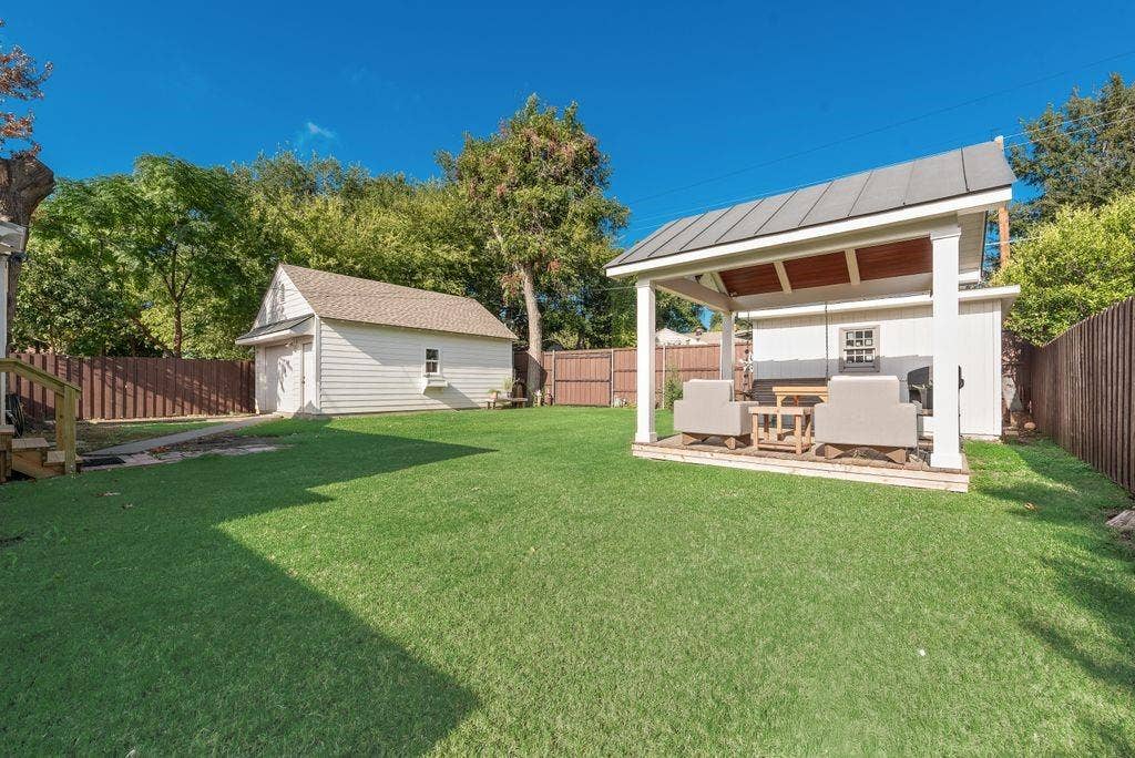 2815 Anzio Drive, Dallas, TX 75224 Backyard featuring a manicured lawn, detached garage, covered patio with a metal roof, and wood-panel fencing