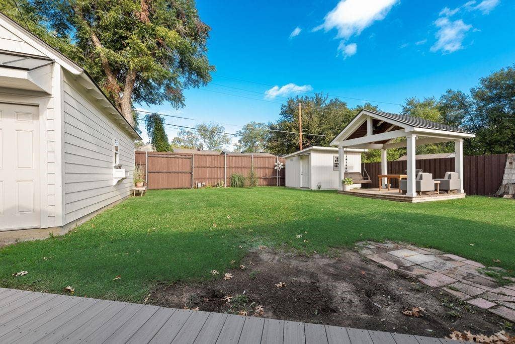 2815 Anzio Drive, Dallas, TX 75224 Expansive backyard featuring a manicured lawn, detached storage structure, covered open-air pavilion, and perimeter wood privacy fencing