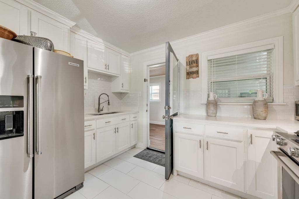 2815 Anzio Drive, Dallas, TX 75224 Kitchen featuring white cabinetry, solid-surface countertops, subway tile backsplash, stainless steel appliances, and large-format tile flooring