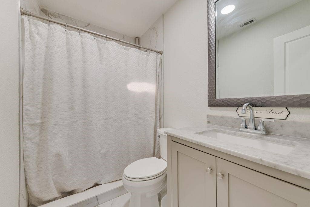 2815 Anzio Drive, Dallas, TX 75224 Bathroom featuring a vanity with stone-top basin, undermount sink, brushed-metal faucet, and a large framed mirror