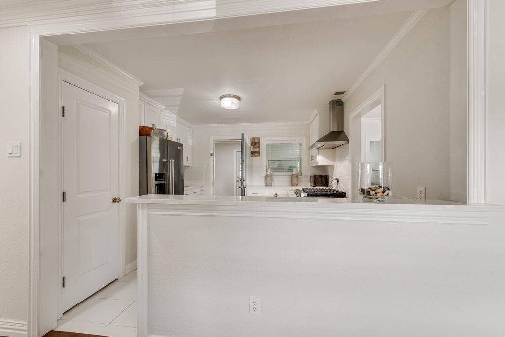 2815 Anzio Drive, Dallas, TX 75224 Kitchen featuring white cabinetry, stainless steel appliances, stone-surface breakfast bar, and stainless steel chimney-style range hood