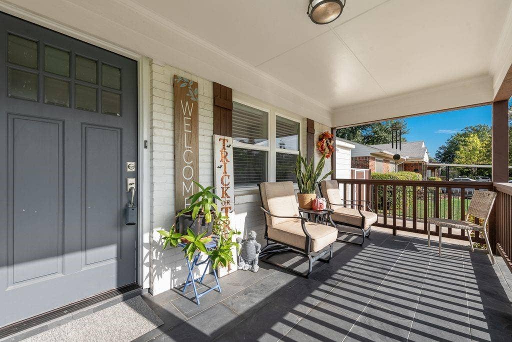 2815 Anzio Drive, Dallas, TX 75224 Covered front porch featuring dark tile flooring, a painted brick exterior, a multi-pane glass entry door, and a wooden balustrade