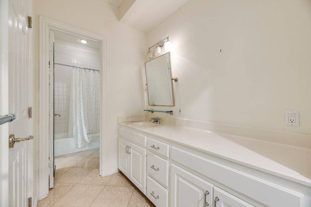1418 Yakimo Drive, Dallas, TX 75208 Extended vanity with solid-surface countertop and integrated sink, white cabinetry with silver-tone hardware, wall-mounted mirror, and ceramic tile flooring