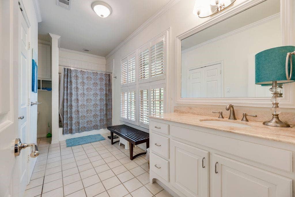 1418 Yakimo Drive, Dallas, TX 75208 Bathroom featuring white cabinetry, light-toned stone countertop, large framed wall mirror, plantation shutters, and ceramic tile flooring