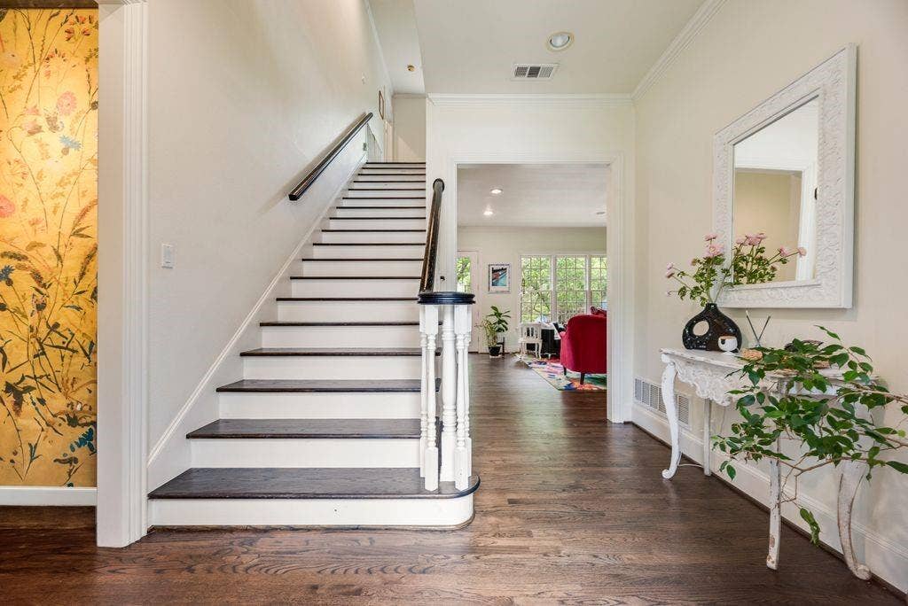 1418 Yakimo Drive, Dallas, TX 75208 Foyer featuring wood-finish flooring, a staircase with dark-stained treads, white risers, and a decorative handrail, and an accent wall with floral wallcovering