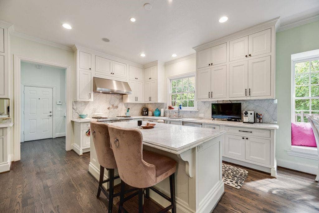 1418 Yakimo Drive, Dallas, TX 75208 Kitchen featuring white shaker cabinetry, stone-surface countertops, full-height stone backsplash, stainless steel range hood, and wood-finish flooring